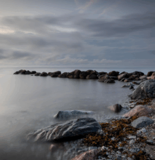 Stenar vid havet i skymningsljus med molnig himmel.