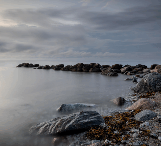 Stenar vid havet i skymningsljus med molnig himmel.