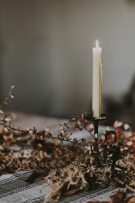 Ett ensamt, långt ljus står i en ljusstake omgiven av torkade blommor.