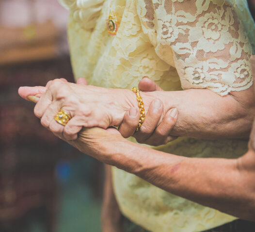 Två äldre personer håller varandras händer, klädda i gula spetskläder.